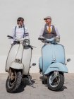 Dreamy middle-aged hipsters in fashionable clothes with retro motorbikes leaning on wall in sunny day — Stock Photo