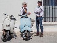 Hipsters positivos de mediana edad en ropa elegante con motos retro hablando entre sí en un día soleado - foto de stock