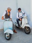 Positive middle-aged hipsters in elegant clothes with retro motorbikes looking at each other in sunny day — Stock Photo