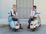 Hipsters positivos de meia-idade em roupas elegantes com motos retro olhando uns para os outros em dia ensolarado — Fotografia de Stock