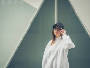 Junge moderne Hipsterin in lässiger Kleidung vor dem Hintergrund einer geometrischen Wand, die in die Kamera blickt — Stockfoto