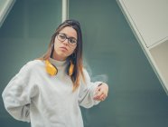 Confiante moderno hipster feminino em roupas casuais e fones de ouvido amarelo brilhante no fundo da parede — Fotografia de Stock