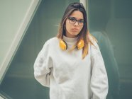 Fiducioso moderno hipster femminile in abiti casual e cuffie giallo brillante sullo sfondo della parete — Foto stock