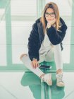 Junge moderne Hipsterin in lässiger Kleidung vor dem Hintergrund einer geometrischen Brille, die in die Kamera blickt — Stockfoto