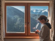 Женщина просматривает смартфон возле окна — стоковое фото