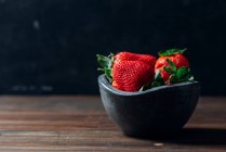 Fresh ripe strawberries in black concrete bowl on wood background — Stock Photo