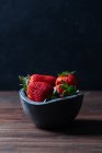 Fresh ripe strawberries in black concrete bowl on wood background — Stock Photo
