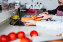 Anonyme enfants peler la carotte tout en cuisinant salade saine dans la cuisine — Photo de stock
