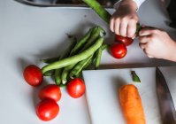 Niño anónimo eligiendo ingredientes para preparar una ensalada saludable en la cocina - foto de stock