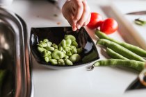 Mano di anonima bambina peeling fagioli maturi durante la cottura di insalata sana in cucina — Foto stock