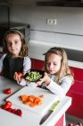 Bambine e ragazzi che tagliano e sbucciano verdure mature mentre cucinano insalata sana in cucina insieme — Foto stock