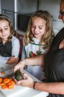 Anonymous adult showing little girls to cook healthy salad in kitchen together — Stock Photo