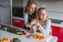 Маленькая девочка демонстрирует половину спелого авокадо на камеру, стоя на кухне и глядя в камеру — стоковое фото
