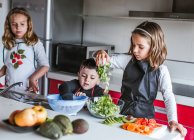 Маленькі дівчата і хлопчик Діти граються, готуючи здоровий салат на кухні разом — стокове фото