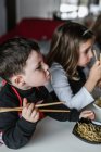 Junge und Mädchen essen leckere Nudeln mit vegetarischen Schnitzeln und Gemüse, während sie zu Hause am Tisch sitzen — Stockfoto