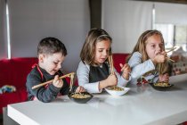 Junge und zwei Mädchen essen leckere Nudeln mit vegetarischen Schnitzeln und Gemüse, während sie zu Hause am Tisch sitzen — Stockfoto
