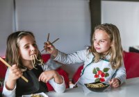 Zwei Mädchen essen leckere Nudeln mit vegetarischen Schnitzeln und Gemüse, während sie zu Hause am Tisch sitzen — Stockfoto