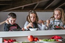 Ragazzo e due ragazze che mangiano gustosi spaghetti con costolette vegetariane e verdure mentre sono seduti a tavola a casa — Foto stock