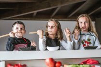 Мальчик и две девочки едят вкусную лапшу с вегетарианскими котлетами и овощами, сидя за столом дома — стоковое фото