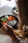 Вид от первого лица анонимной девушки, которая ест вегетарианские котлеты и овощи, сидя за столом дома — стоковое фото