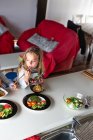 Menina comendo costeletas e legumes vegetarianos enquanto se senta à mesa em casa — Fotografia de Stock