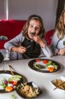 Menina comendo costeletas e legumes vegetarianos enquanto se senta à mesa em casa — Fotografia de Stock