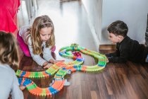 Хлопчик і дві дівчини грають з машинами та іграшковою дорогою на паркетній підлозі вдома разом — стокове фото