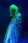 Junge Asiatin mit gelber Perücke und transparentem Kunststoffanzug posiert in Leuchtstoffröhren — Stockfoto