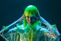 Young Asian woman in yellow wig and transparent plastic wear posing in fluorescent light — Stock Photo