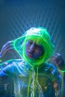 Молодая азиатка в жёлтом парике и прозрачном пластиковом износе позирует в флуоресцентном свете — стоковое фото