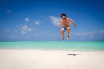 Homem pulando perto do mar azul-turquesa — Fotografia de Stock