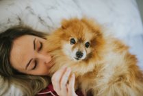 Young happy smiling attractive woman in pajamas lying in bed with little fluffy dog — Stock Photo