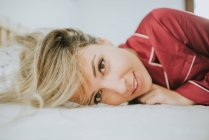 Веселая молодая красивая женщина в пижаме, улыбающаяся на кровати в спальне — стоковое фото