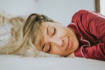 Giovane bella donna in pigiama sorridente mentre dorme sul letto in camera da letto — Foto stock