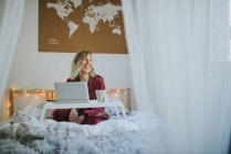 Молодая красивая женщина в пижаме сидит в постели с кофе и цифровой планшет на подносе — стоковое фото