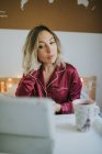 Молода красива жінка в піжамі дивиться на планшет, сидячи в ліжку з кавою на столі лоток — стокове фото