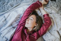 Jeune jolie femme en pyjama souriant tout en se relaxant au lit — Photo de stock