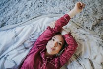 Junge hübsche Frau im Schlafanzug lächelt, während sie es sich auf dem Bett gemütlich macht — Stockfoto