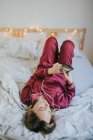 Jovem mulher bonita de pijama deitada na cama e usando smartphone — Fotografia de Stock
