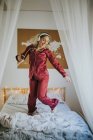 Young happy smiling woman in pajamas with headphones dancing on bed in morning — Stock Photo
