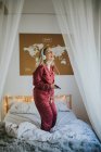 Jeune femme souriante heureuse en pyjama avec écouteurs dansant sur le lit le matin — Photo de stock