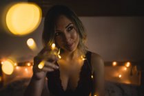 Young elegant woman in underwear sitting in bed surrounded with light garland — Stock Photo