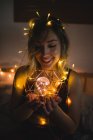 Young woman in underwear sitting in bed surrounded with light garland and holding light bulb — Stock Photo