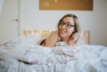 Mujer joven en anteojos y ropa interior acostada en la cama por la mañana - foto de stock