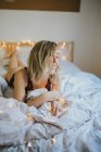 Jovem mulher de roupa interior deitada na cama com luzes — Fotografia de Stock