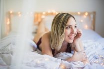 Jovem mulher de roupa interior deitada na cama com luzes — Fotografia de Stock