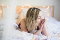 Jovem sonhadora de roupa interior deitada na cama com luzes — Fotografia de Stock