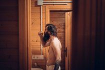 Side view of manly hipster with tattoo and beard brushing teeth while resting in wooden cabin — Stock Photo