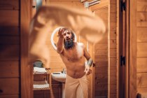 Hipster de moda con torso desnudo tirando toalla después de tener ducha en casa de campo de madera - foto de stock