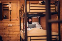 Homme utilisant un ordinateur portable dans un lit superposé rustique — Photo de stock
